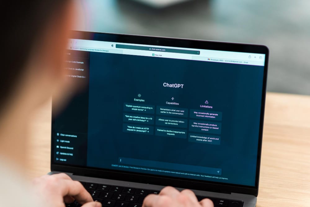Person using ChatGPT on a laptop — the homepage interface showing examples, capabilities, and limitations of the AI assistant