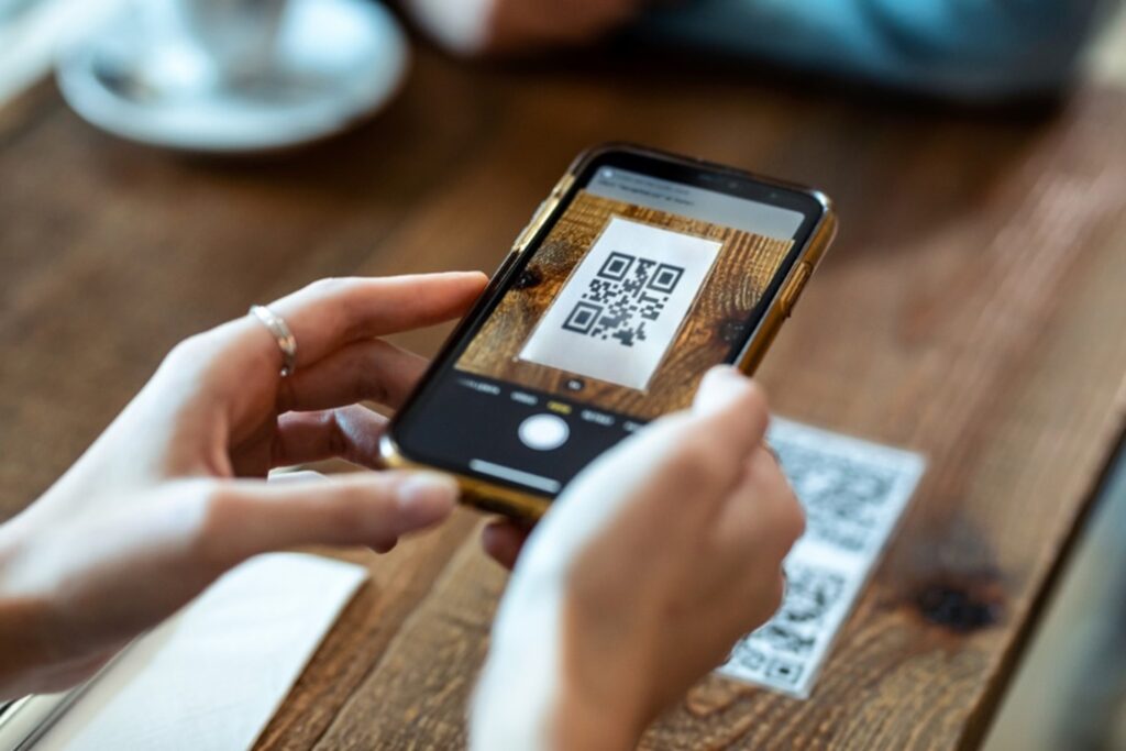 Close-up of hands holding a smartphone scanning a QR code from a printed card or screen, brand-neutral