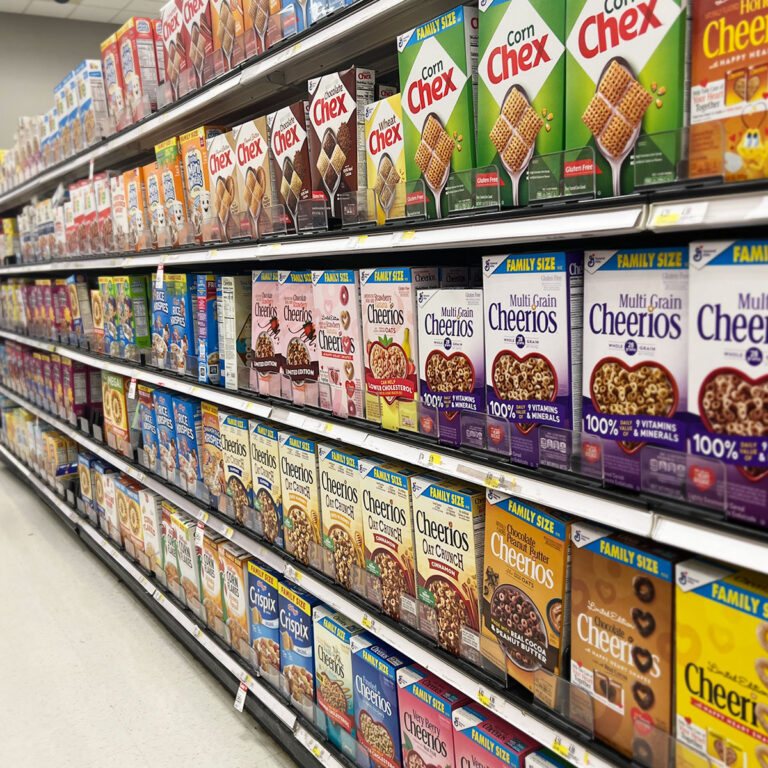 Aisle of brightly packaged ultra‑processed foods, including cereals, snacks, and sodas, with shallow depth of field.