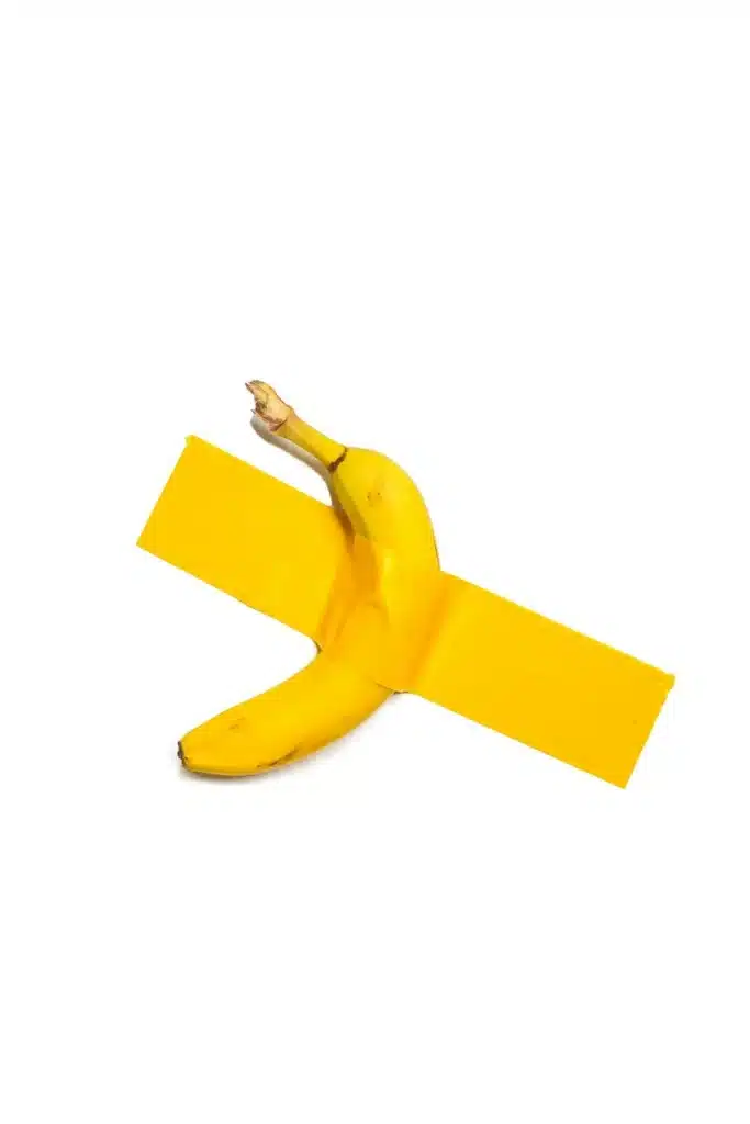 Banana duct-taped to a gallery-style wall with colored tape, minimal and brand-neutral conceptual photograph.